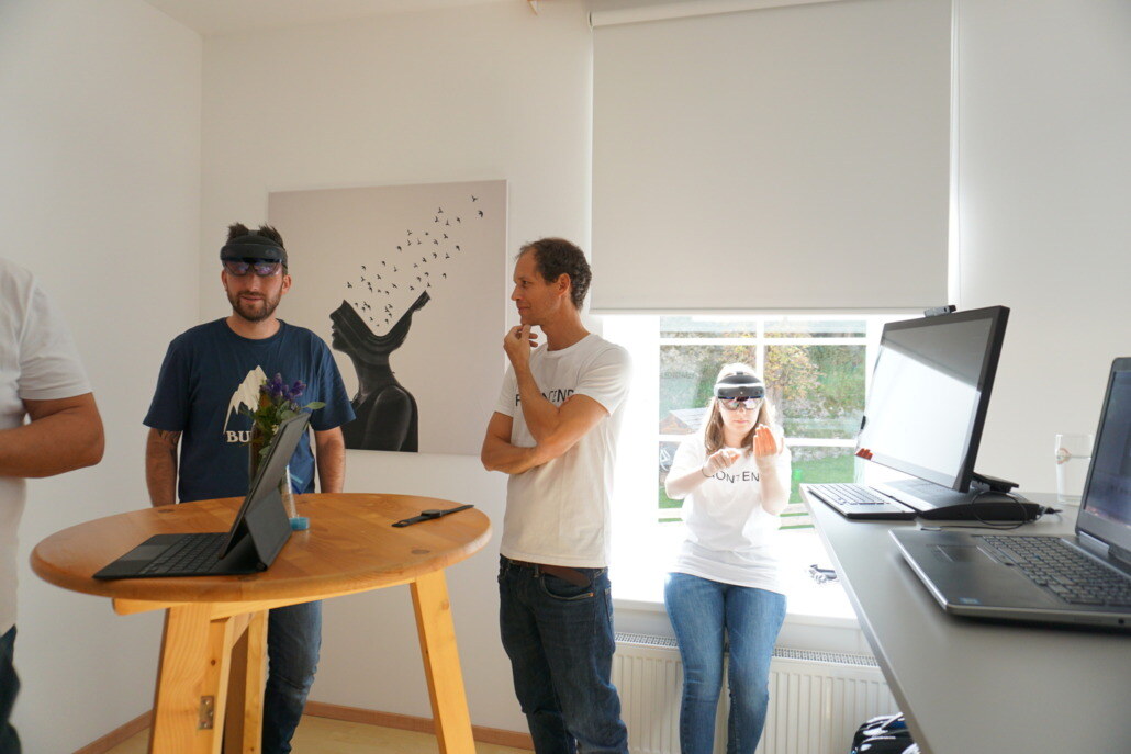 Two colleagues are trying out HoloLenses at the opening of the new Kärnten location. They are wearing the AR glasses and interacting with virtual content in a curious and excited atmosphere.