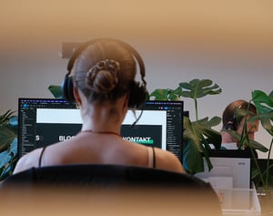 Frau mit Kopfhörern arbeitet konzentriert an Web- und Softwareprojekten in einem hellen, modernen Büro mit Pflanzen.