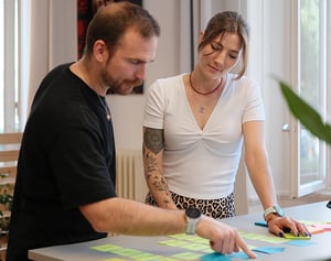 Zwei Personen arbeiten gemeinsam an einem Tisch mit farbigen Post-its in einem hellen Büro – sie besprechen Ideen und gestalten ein Konzept.